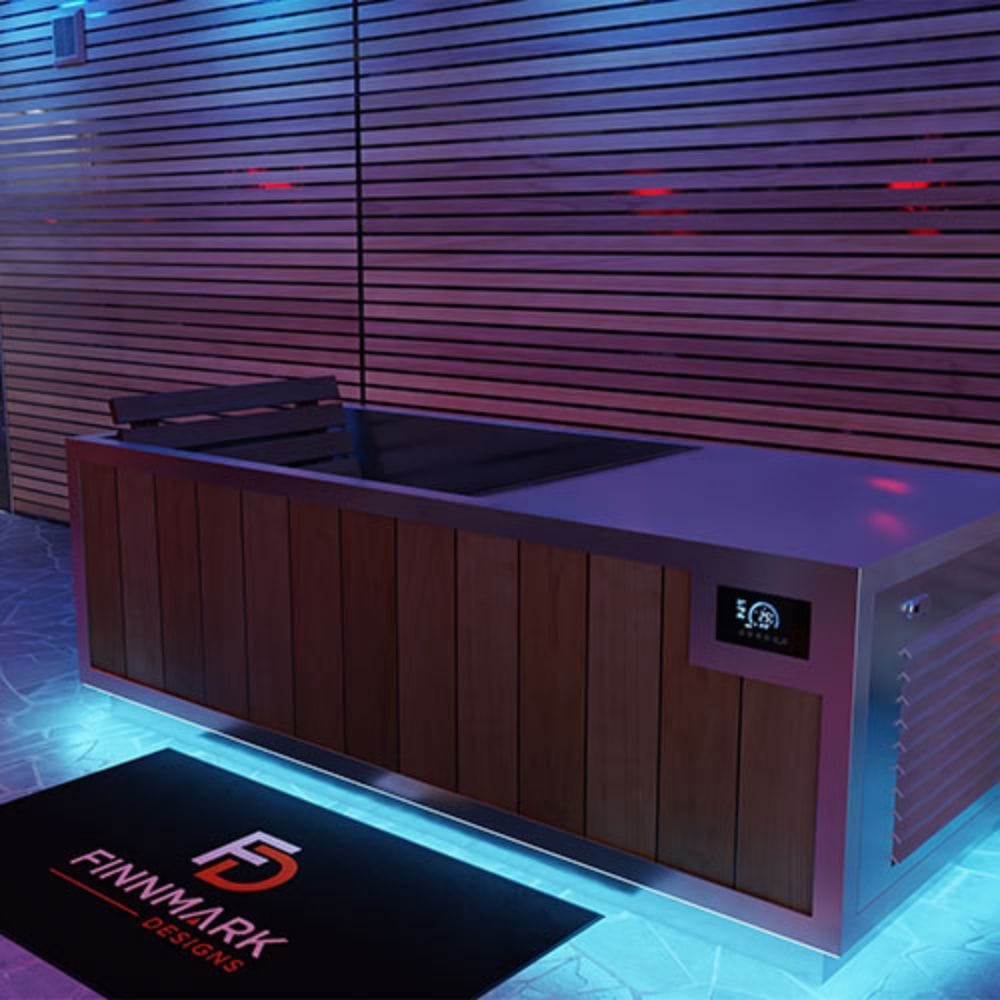A modern outdoor hot tub with a wood-paneled exterior and stainless steel trim, set against a slatted wall with ambient purple lighting. A black mat with the 'FINNMARK DESIGNS' logo is placed in front of the tub.