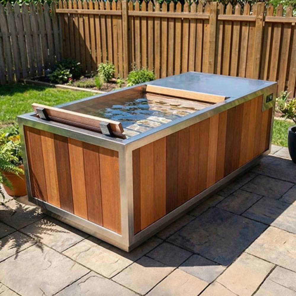 A rectangular outdoor hot tub or plunge pool with a wood-look exterior and stainless steel trim, shown on a stone patio in a backyard with a wooden fence and grass.