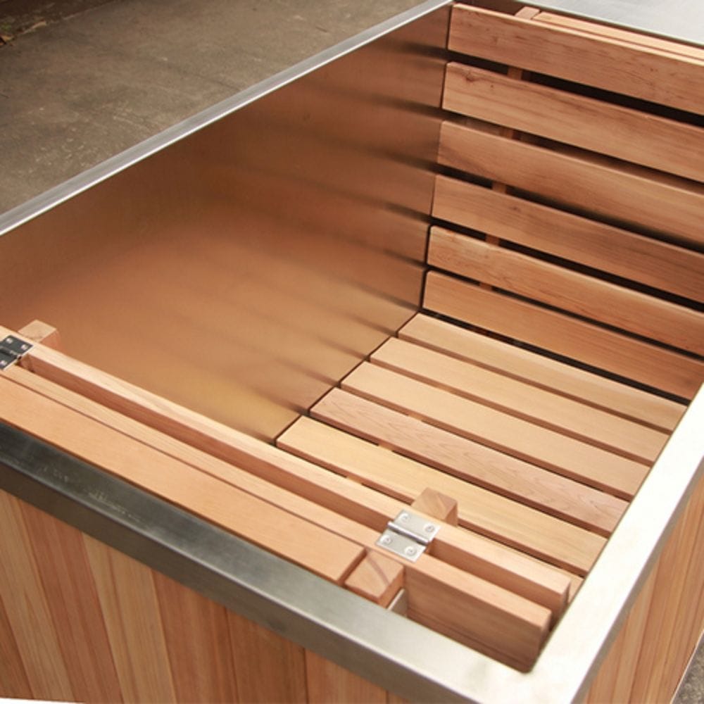 Close-up of a wooden hot tub or sauna interior with light natural wood slats and a brushed metal rim, shown in a warehouse-like setting.