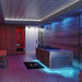 A modern indoor spa or wellness room featuring a large stainless steel and wood sauna/steam unit, a glass shower enclosure, a red sauna compartment, patterned flooring, and ambient blue and purple lighting.
