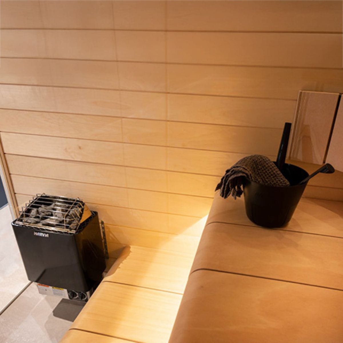 Wooden sauna interior with a black bucket and towel and Harvia sauna heater