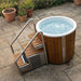 Wooden hot tub with a ladder on a stone patio