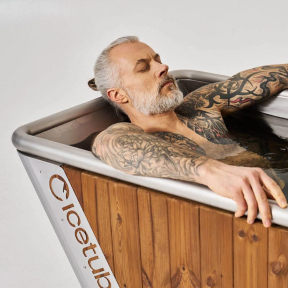 Man with tattoos relaxing in a wooden bathtub labeled 'Cicetub'