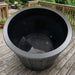 Black plastic planter on a wooden deck with outdoor furniture in the background
