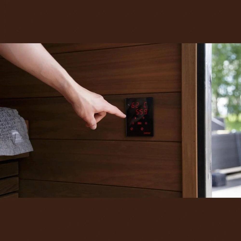 Hand adjusting a digital sauna temperature control panel on wooden sauna walls.